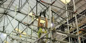Construction worker wearing a safety harness adjusting metal scaffolding inside an industrial structure.
