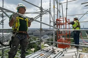 Construction workers wearing safety harnesses working on scaffolding at a high-rise building site.