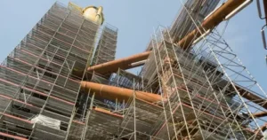 Industrial structure surrounded by scaffolding and large pipes.
