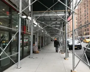 Pedestrians walking under sidewalk scaffolding in a city.