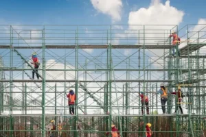 Construction workers assembling metal scaffolding at a building site under a blue sky